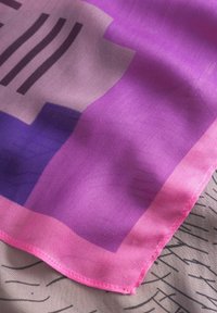 Zijden sjaal met een mengeling van paarse en roze tinten, afgewerkt met abstracte geometrische patronen en een gladde textuur. De randen zijn roze gestikt.