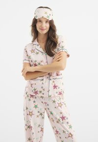 Conjunto de pijama rosa con un patrón de estrellas en varios colores, con mangas cortas, un cuello con solapa y una máscara para los ojos a juego.