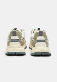 Sneakers w kolorze kremowym i beżowym, wykonane ze skóry i zamszu. Projekt obejmuje fakturowaną podeszwę z drobnymi kropeczkami oraz pętle do chwytania.