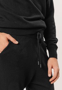 Schwarzer Strickpullover und passende Hose mit Zugbandbund, die eine weiche Textur und gerippte Bündchen aufweist. Taschen an der Hose für praktische Funktionen.