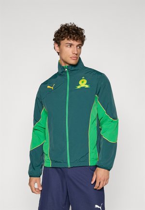 Grüne und blaue Sportjacke mit gelben Akzenten. Verfügt über einen hohen Kragen, einen durchgehenden Reißverschluss und ein Logo auf der Brust. Leichtes, lässiges Design.