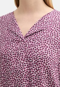 Lila und weiß gemusterte Bluse mit V-Ausschnitt, kurzem Kragen und Knopfleiste, aus leichtem Stoff mit weicher Textur.