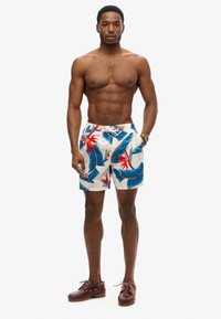Bañador masculino en una tela ligera con un vibrante patrón tropical de hojas azules y flores rojas, cintura elástica y cordón.