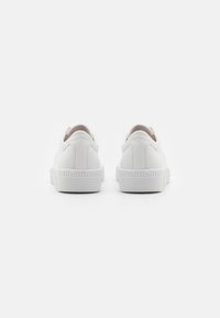 Weiße Sneakers mit einem strukturierten Leder-Obermaterial, abgerundetem Absatz und Gummisohle mit vertikalen Rillen. Minimalistisches Design ohne sichtbare Logos.