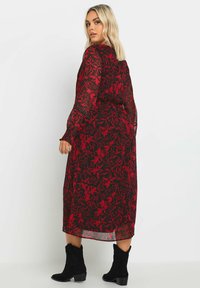 Lång, genomskinlig svart klänning med röd blommönster, långa ärmar, volangärmar och ett åtdraget midja. Bärs med svarta ankelboots.