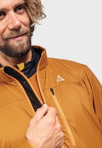 Veste isolante orange avec un col montant, fermeture éclair à l'avant et un logo. Comprend une doublure intérieure noire contrastante et une poche sur le côté.