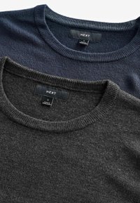 Deux pulls à col rond empilés ; l'un bleu marine foncé, l'autre gris charbon. Les deux présentent des poignets côtelés et des étiquettes indiquant la taille et la marque.