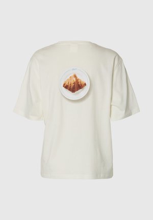 T-shirt couleur crème avec une impression centrée au dos représentant un croissant sur une assiette blanche sur un fond uni.