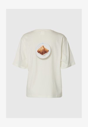 T-shirt couleur crème avec une impression centrée au dos représentant un croissant sur une assiette blanche sur un fond uni.