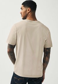 Camiseta corta de manga de color beige hecha de tejido suave, con un cuello redondo y un corte holgado, combinada con jeans de mezclilla oscura.