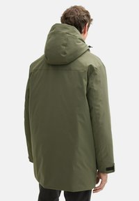 Zelená, polstrovaná parka s kapucňou; má rovný strih, hladkú textúru a nastaviteľné manžety s suchými zipsami. Zobrazený pohľad zozadu.