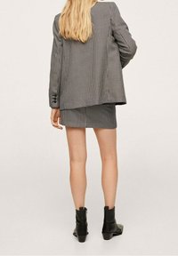 Blazer de cuadros blancos y negros a juego con minifalda, tela texturizada, corte entallado, con una silueta relajada y botas negras hasta el tobillo.