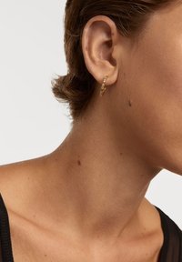Guldørering i hoop-stil med et struktureret, snoet design, prydet med små klare detaljer. Anbragt på en models øre, som viser dens glans og detaljer.
