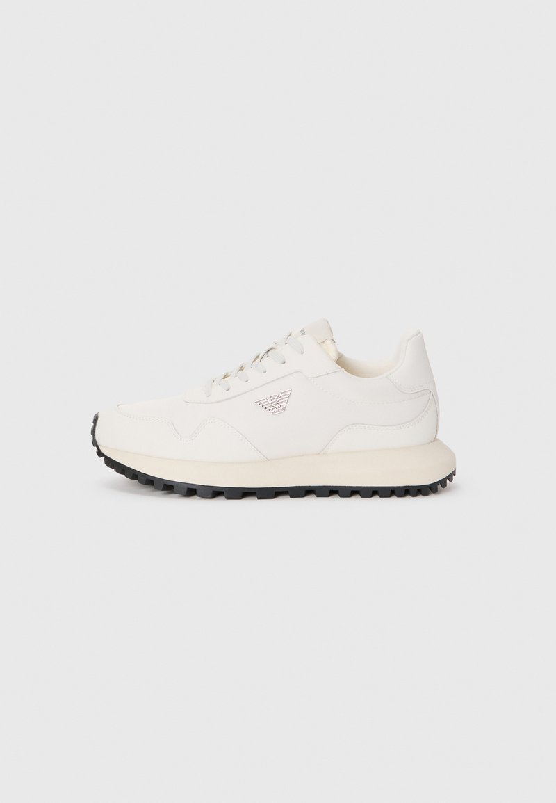 Sapatilha branca com um cabedal de couro liso, realces texturizados nas laterais e uma sola de borracha preta. Apresenta um logótipo na lateral e atacadores grossos.