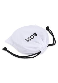 Λευκή τσάντα με κορδόνι που φέρει τη λέξη "BOSS" με έντονα μαύρα γράμματα. Κατασκευασμένη από ύφασμα, έχει υφή στην επι φάνεια και μαύρα κορδόνια ως διακοσμητικά στοιχεία.