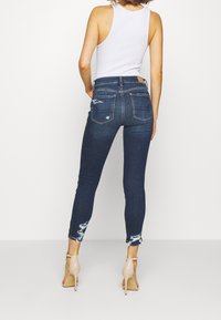 Smala jeans i mörk tvättad denim med slitna detaljer vid fållen och fickorna. Kombinerat med en vit tanktop och nakna högklackade skor.