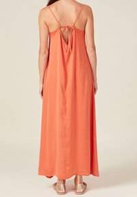 Maxikleid in Korallenorange, aus weichem Stoff gefertigt. Mit dünnen Trägern, einer gebundenen Rückenschließe und einer fließenden Silhouette. Mit offener Rückendetail akzentuiert.