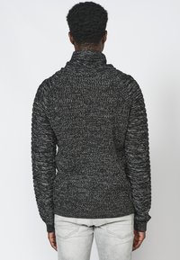 Maglione lavorato a maglia nero e grigio con colletto alto, polsini a coste e corpo testurizzato; presenta motivi verticali sulle maniche.