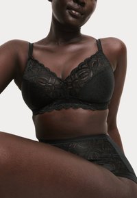 Zwarte kanten bralette met golvende randen, gestippelde textuur en delicate bloemenaccenten, gecombineerd met hoge kanten onderbroek.