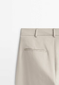 Beige broeken met een gladde textuur, voorzien van een tailleband, riemlussen en een enkele achterzak met een gepiped opening.