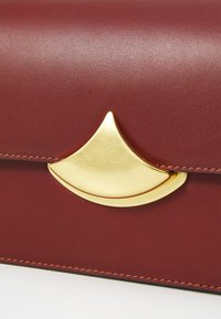 Borsa in pelle bordeaux con chiusura in tono oro e design curvo, con cuciture a contrasto lungo i bordi.