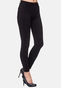 Jean skinny noir en denim, avec taille haute, ourlet déchiré et poches avant. Associé à des escarpins noirs.