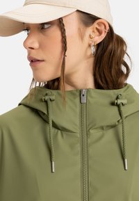Olive green jacket with a zip closure, adjustable hood, and textured drawstrings; features metallic hardware and a smooth, lightweight fabric.