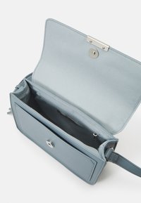 Piccola borsa blu chiaro con pattina magnetica, tasca interna con zip e tracolla regolabile, mostrata aperta e vuota su sfondo bianco.