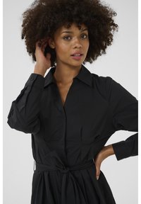 Black shirt dress made of lightweight fabric, featuring a classic collar, long sleeves, a tied waist, and a pleated skirt design.