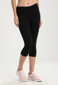 Leggings capri negros con una cinturilla ancha y doblada, confeccionados en una tela elástica. Combinados con zapatillas deportivas rosa claro con detalles en blanco.