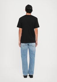 Svart bomulls t-skjorte med korte ermer, kombinert med lyseblå jeans. Denimet har en falmet tekstur og rett passform, fullført med svarte sko.