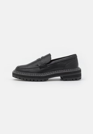 Mocassin en cuir noir avec semelle épaisse rayée et surpiqûres blanches, avec une lanière sur le dessus et un dessin de semelle robuste.