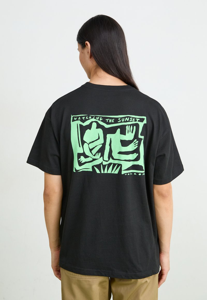 T-shirt en coton noir avec une impression graphique verte au dos, comportant des formes abstraites et le texte "REGARDER LE SOLEIL SE COUCHER."