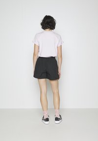 Maglietta rosa a maniche corte, pantaloni corti neri, calzini rosa a fantasia e sneaker nere. L'outfit ha un design casual e sportivo.