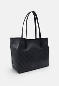 Zwarte tote bag met subtiele gedetailleerde logo-ontwerp en lange schouderbanden tegen een witte achtergrond.