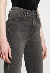 Höga grå jeans i denim med en figurnära silhuett, synlig sömnad och en liten slitage-detalj vid låret.