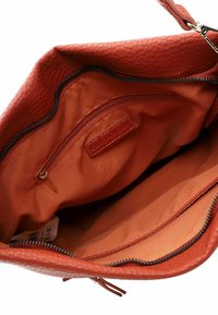 Sac fourre-tout avec un extérieur en cuir rouge texturé. L'intérieur présente une doublure en tissu orange, une poche zippée et une étiquette de marque.