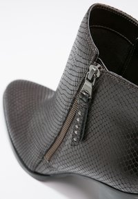 Stivale alla caviglia marrone scuro con finitura in pelle a effetto rettile, dotato di zip laterale e dettagli cuciti, punta leggermente affusolata.