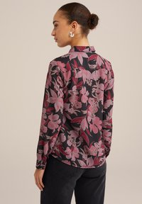 Blusa a maniche lunghe, base nera con grande motivo floreale rosa, tessuto morbido, colletto, vestibilità comoda, cuciture visibili, spacco laterale all'orlo.