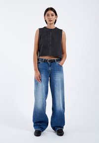 Zwart denim mouwloos topje met een ruwe rand, gecombineerd met lichtblauwe wijde jeans met een vervaagde wassing en een zwarte riem.