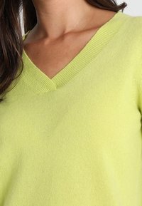 Limegrön v-ringad tröja gjord av mjukt, strukturerat tyg, med ribbat halsband och slät kropp.