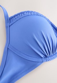 Haut de bikini rembourré bleu avec détail de tissu froncé et bretelle réglable sur fond neutre.