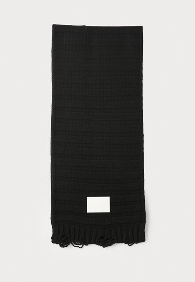 Bufanda negra con un patrón de rayas texturizadas, terminada con flecos en los extremos, que cuenta con una pequeña etiqueta blanca. Material de punto ligero.