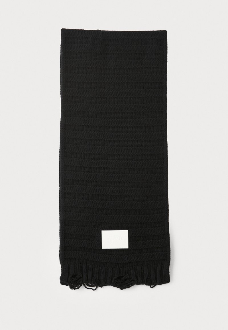 Must mustriba lõngaga, millel on tekstuuriga triibuline muster, lõpetatud franjedega otstes, millel on väike valge silt. Kerge kudumismaterjal.