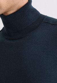 Maglione a collo alto di color navy con texture a maglia stretta e colletto a coste, che presenta linee pulite e un design minimalista.