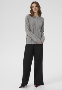 Siv izdelan kardigan z okruglim ovratnikom, zapenjanjem na gumb in rebrastimi manšeti, v kombinaciji s črnimi širokimi hlačami in bordo špicastimi petami.