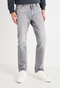 Vaqueros de mezclilla gris claro con corte recto, cinco bolsillos y una cintura clásica, combinados con zapatillas blancas. Textura suave y mínimo desgastado.