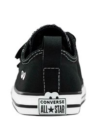 Zapatilla de lona negra con suela de goma blanca, que presenta un parche de logo, costuras de acento y dos detalles en el talón.