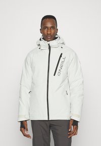 Witte geïsoleerde jas met een hoge kraag, verstelbare capuchon, ritszakken en zwarte accenten. Materiaal lijkt glad met een matte afwerking.