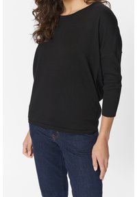 Pull ample noir à col large et manches trois-quarts ; texture côtelée aux manches et à l'ourlet. À associer avec un jean bleu foncé.